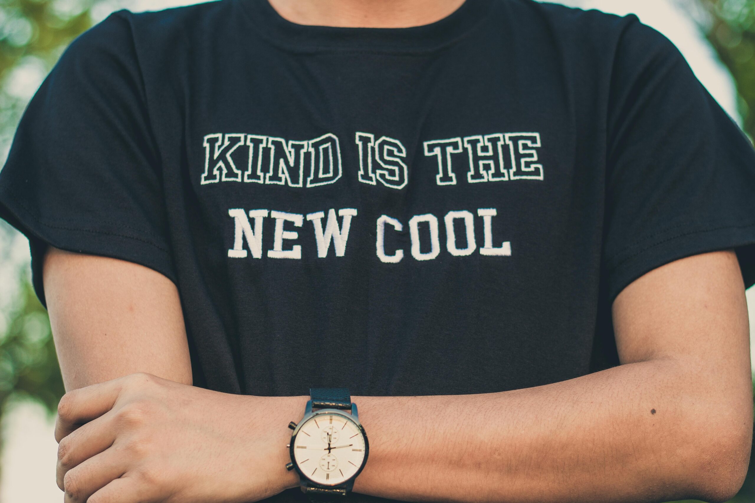 A person wearing a T-shirt with 'Kind is the New Cool' and a stylish wristwatch.